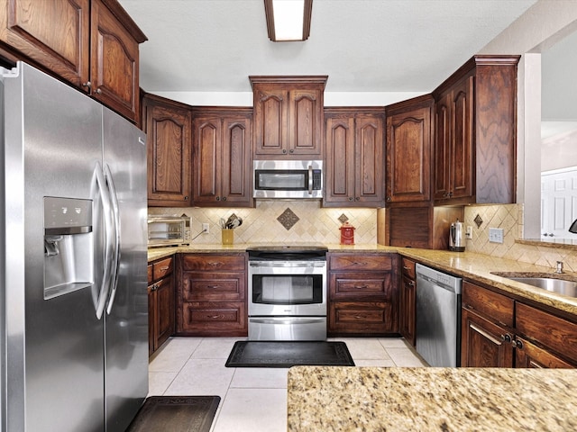 kitchen with light tile patterned flooring, sink, tasteful backsplash, appliances with stainless steel finishes, and light stone countertops