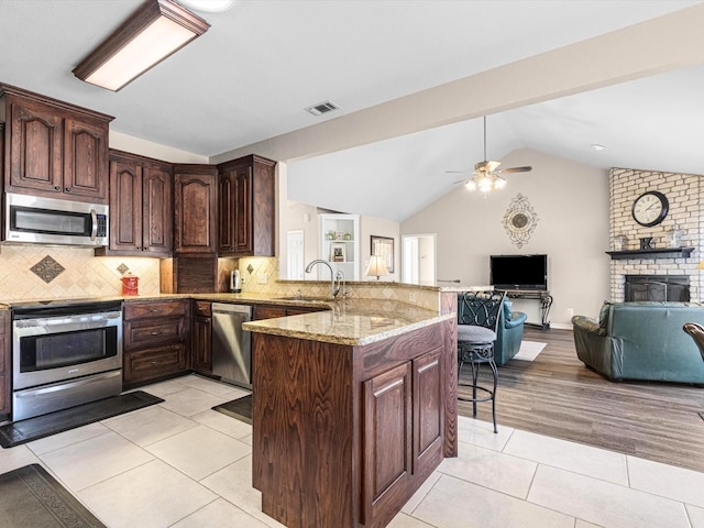 kitchen featuring sink, stainless steel appliances, decorative backsplash, vaulted ceiling, and kitchen peninsula