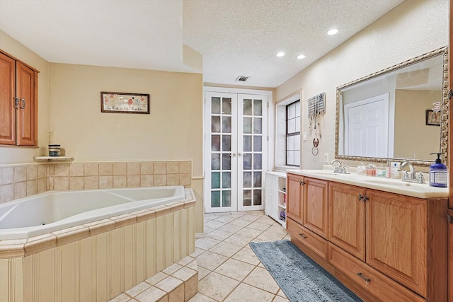 bathroom with tiled bath, tile patterned flooring, french doors, a textured ceiling, and vanity