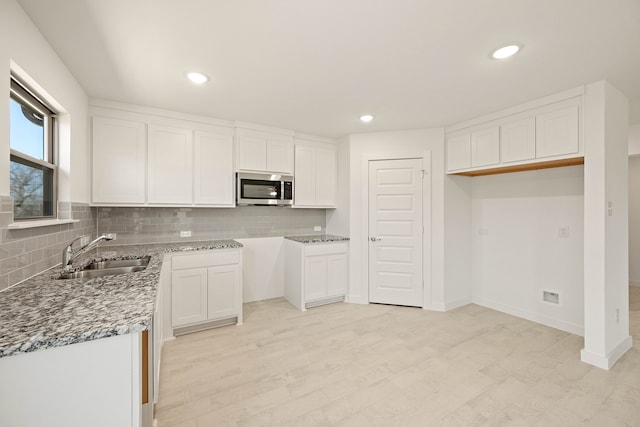 kitchen with sink, white cabinetry, stone counters, light hardwood / wood-style floors, and decorative backsplash