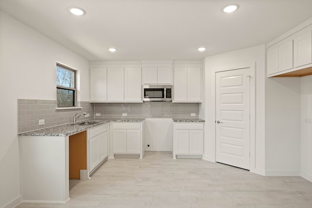 kitchen with sink, light hardwood / wood-style flooring, light stone counters, white cabinets, and decorative backsplash