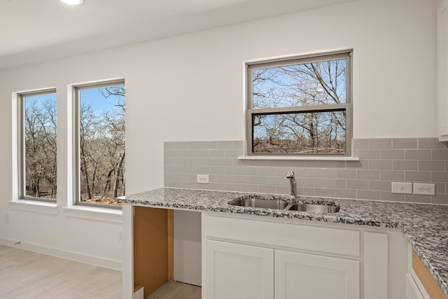 kitchen with white cabinetry, sink, light stone counters, and tasteful backsplash