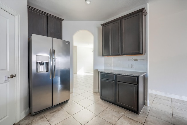 kitchen featuring stainless steel fridge with ice dispenser, dark brown cabinets, and light stone countertops