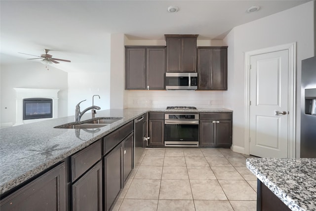 kitchen with light stone countertops, stainless steel appliances, light tile patterned floors, ceiling fan, and sink