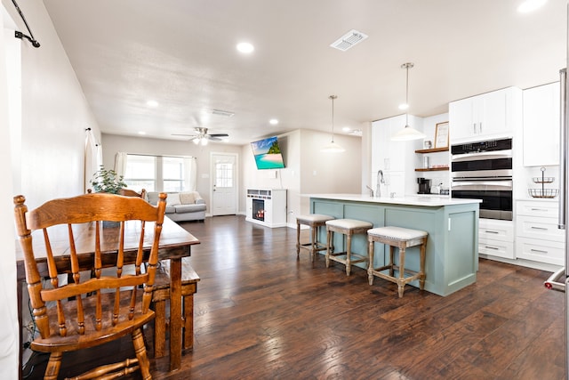 kitchen featuring ceiling fan, white cabinets, decorative light fixtures, and a center island with sink