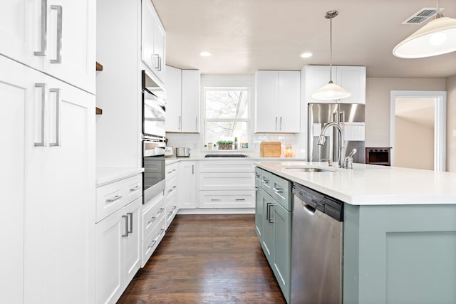 kitchen featuring hanging light fixtures, stainless steel appliances, a kitchen island with sink, white cabinetry, and sink