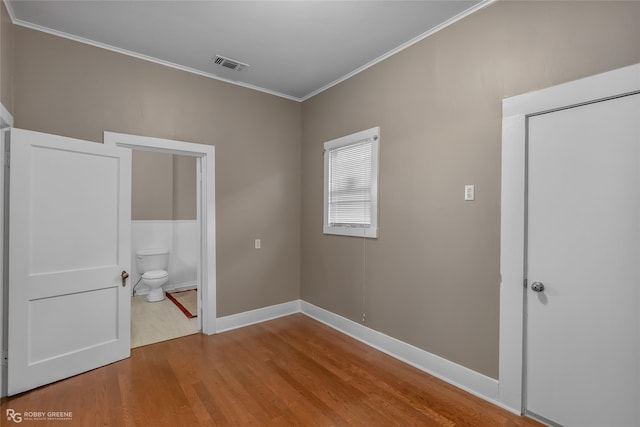 unfurnished bedroom featuring hardwood / wood-style floors, crown molding, and connected bathroom