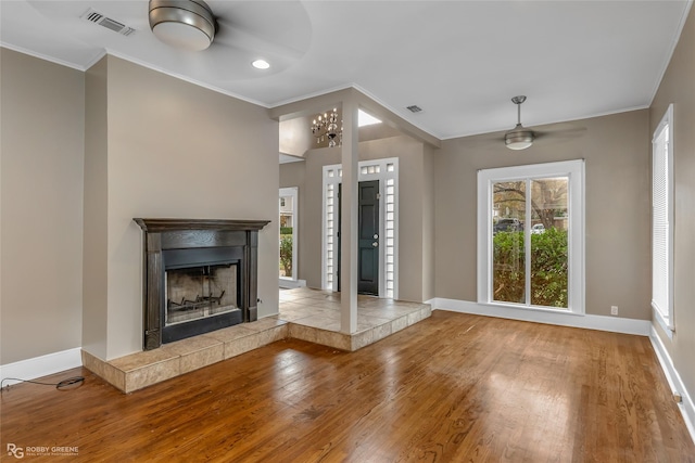 unfurnished living room featuring ornamental molding, a fireplace, ceiling fan with notable chandelier, and wood-type flooring