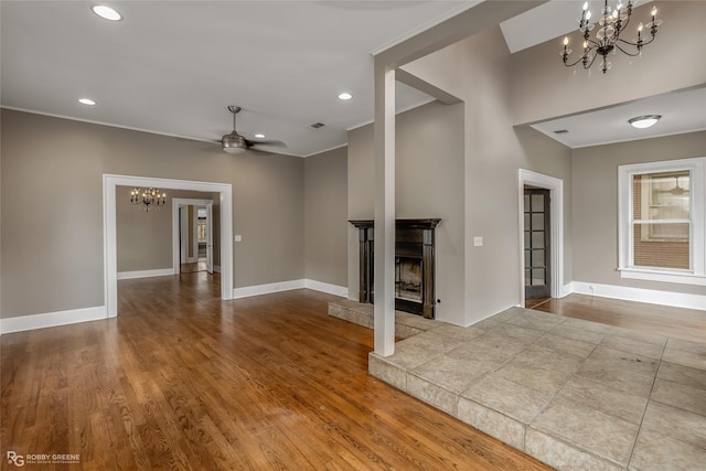 unfurnished living room with ceiling fan with notable chandelier, a tile fireplace, and light hardwood / wood-style floors