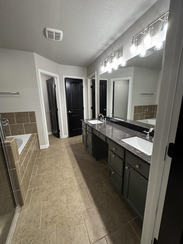 bathroom with a textured ceiling, tiled bath, and vanity