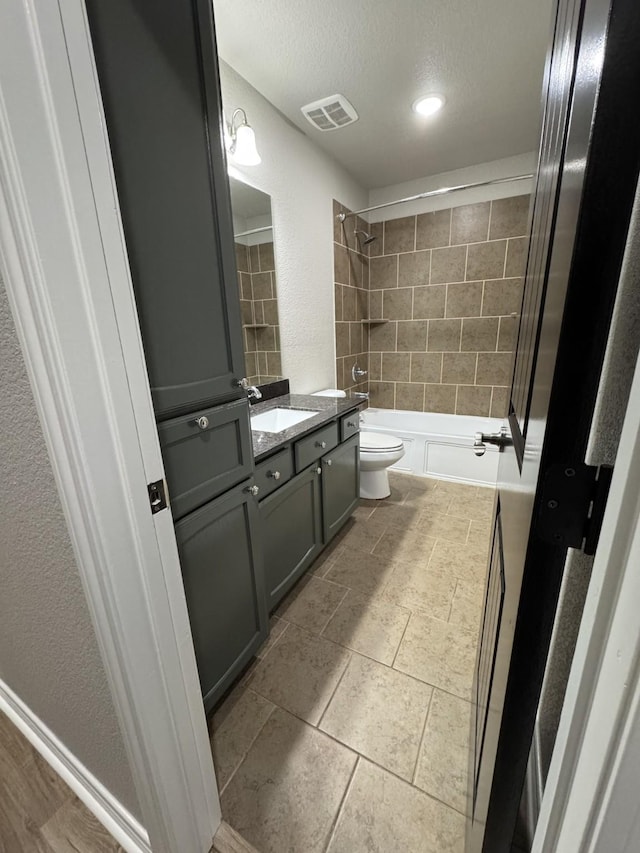 full bathroom with a textured ceiling, vanity, tiled shower / bath combo, and toilet