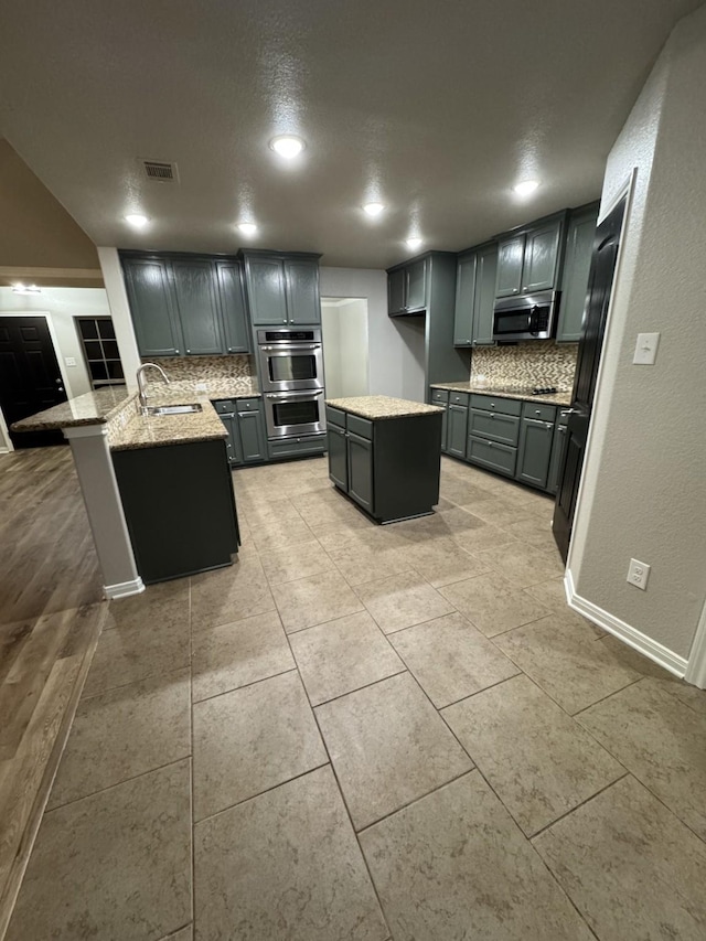 kitchen with stainless steel appliances, light stone countertops, a kitchen island, sink, and tasteful backsplash