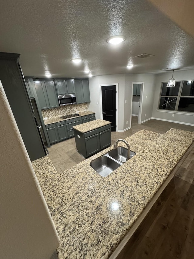 kitchen featuring sink, a kitchen island, a textured ceiling, and light stone counters