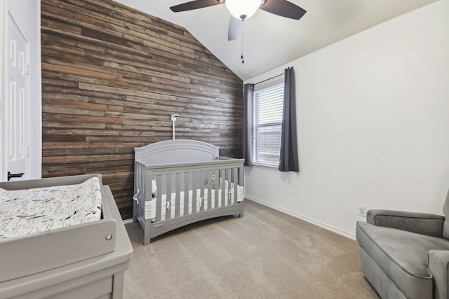 carpeted bedroom featuring ceiling fan, wooden walls, vaulted ceiling, and a crib