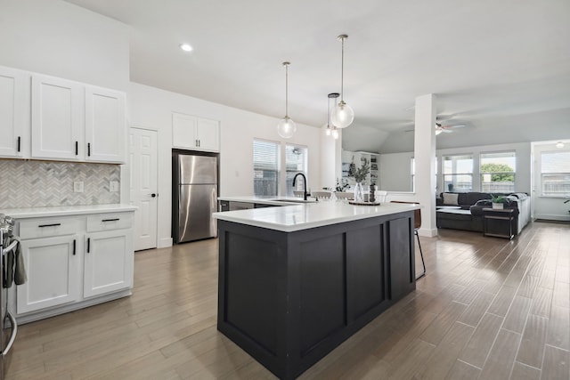 kitchen featuring a kitchen island with sink, stainless steel refrigerator, white cabinets, lofted ceiling, and sink