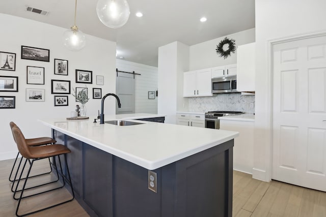 kitchen with white cabinetry, a kitchen island with sink, a barn door, and appliances with stainless steel finishes