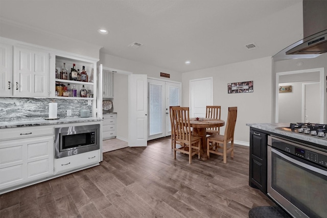 kitchen with stainless steel appliances, white cabinetry, tasteful backsplash, light stone countertops, and wall chimney range hood