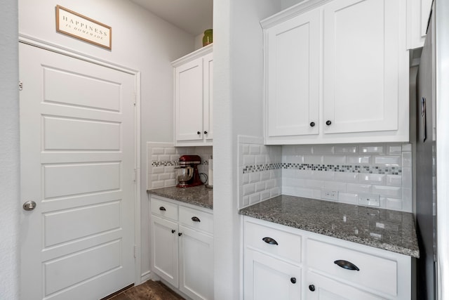 kitchen featuring stainless steel refrigerator, white cabinetry, dark stone countertops, and tasteful backsplash