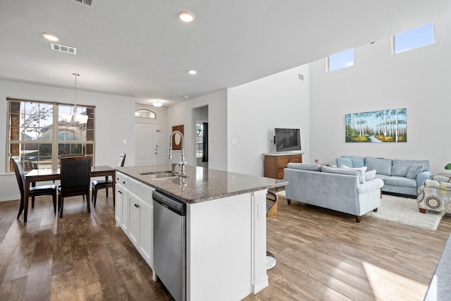 kitchen featuring sink, white cabinets, stainless steel dishwasher, dark stone counters, and a center island with sink