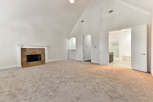 unfurnished living room featuring a tiled fireplace, light colored carpet, high vaulted ceiling, and crown molding