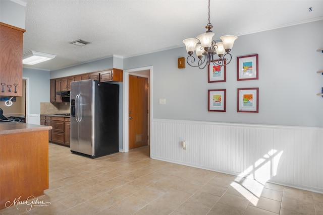 kitchen with a textured ceiling, hanging light fixtures, a notable chandelier, stainless steel fridge, and ornamental molding