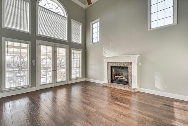 unfurnished living room with dark hardwood / wood-style floors, a high ceiling, french doors, a brick fireplace, and crown molding