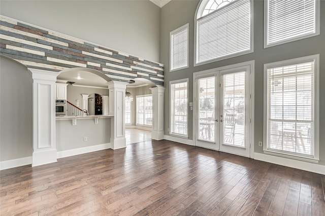 unfurnished living room featuring wood-type flooring, ornamental molding, a wealth of natural light, and decorative columns