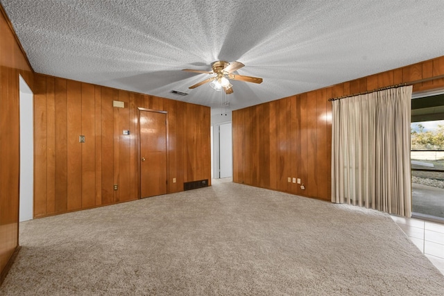 spare room with ceiling fan, light colored carpet, wooden walls, and a textured ceiling