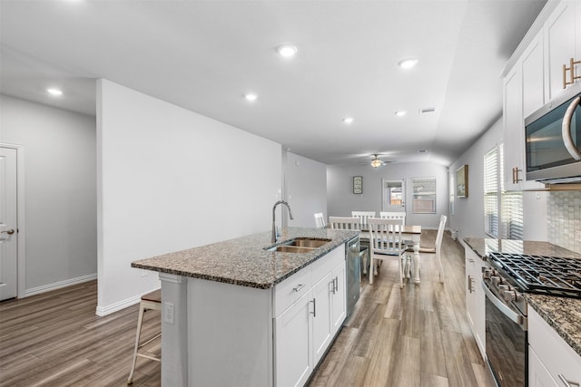 kitchen with sink, stainless steel appliances, white cabinets, ceiling fan, and a center island with sink