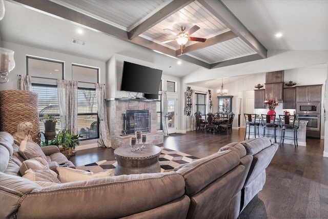 living area with visible vents, dark wood-style flooring, vaulted ceiling with beams, a fireplace, and ceiling fan with notable chandelier