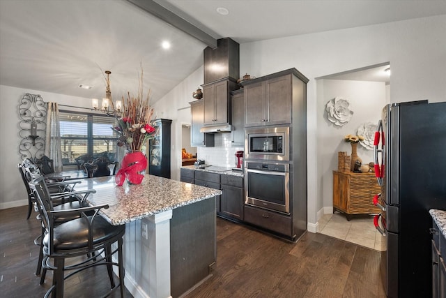 kitchen with light stone counters, dark brown cabinetry, stainless steel appliances, dark wood-style floors, and a kitchen bar