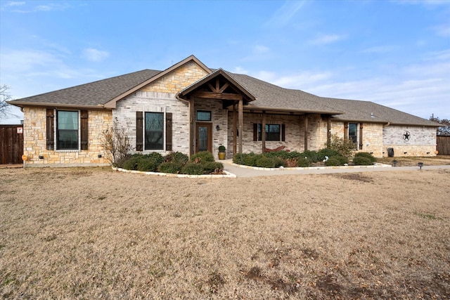 view of front of property featuring stone siding, a shingled roof, fence, and a front lawn