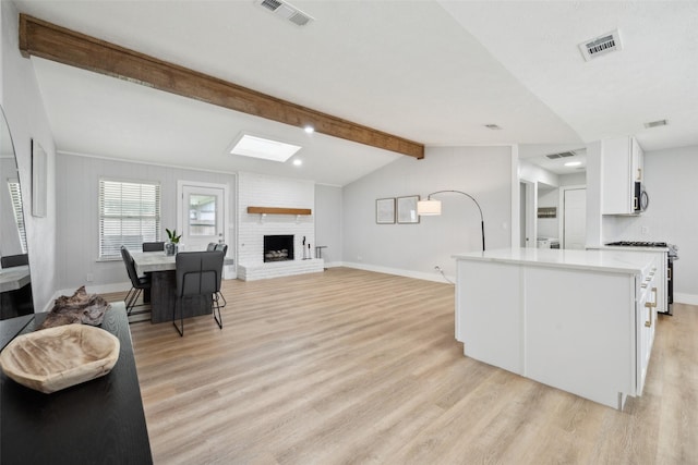 kitchen with lofted ceiling with beams, stainless steel range with gas cooktop, light wood-type flooring, white cabinetry, and a fireplace