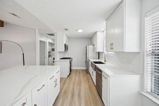 kitchen featuring stainless steel appliances, light wood-type flooring, washing machine and dryer, light stone counters, and white cabinets