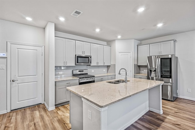 kitchen featuring sink, stainless steel appliances, a kitchen island with sink, and light stone countertops