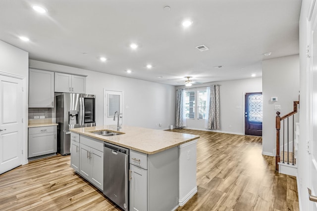 kitchen with light hardwood / wood-style flooring, stainless steel appliances, a kitchen island with sink, backsplash, and sink