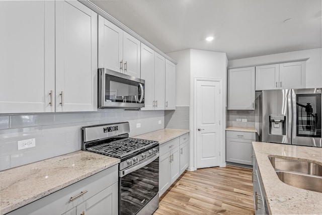 kitchen with stainless steel appliances, white cabinetry, light stone counters, light hardwood / wood-style floors, and tasteful backsplash