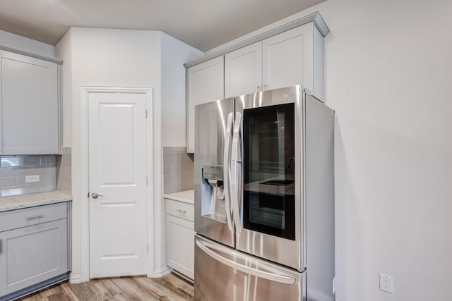 kitchen featuring light stone counters, light hardwood / wood-style flooring, decorative backsplash, stainless steel refrigerator, and gray cabinetry