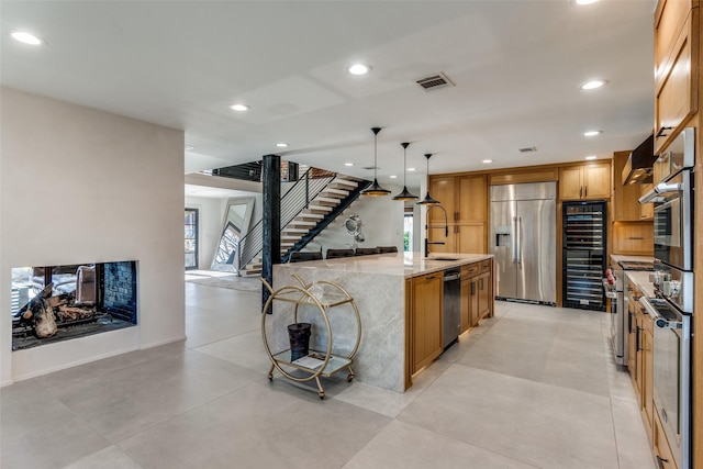 kitchen featuring stainless steel appliances, pendant lighting, light stone counters, a spacious island, and sink