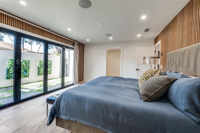 bedroom with access to outside, wooden walls, and light hardwood / wood-style floors