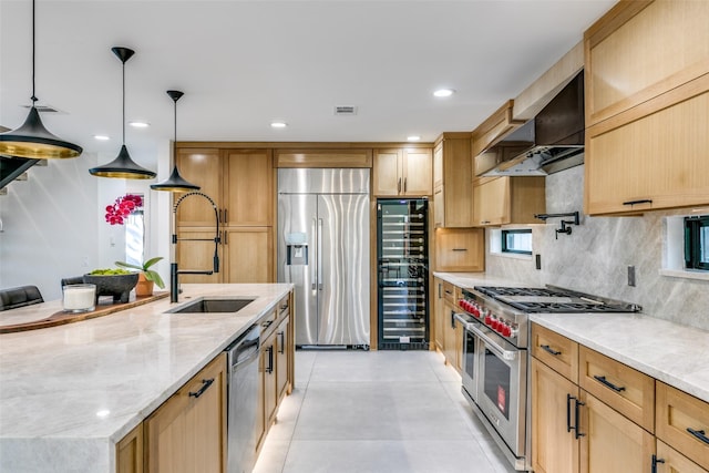 kitchen featuring stainless steel appliances, light stone countertops, sink, wall chimney range hood, and decorative light fixtures