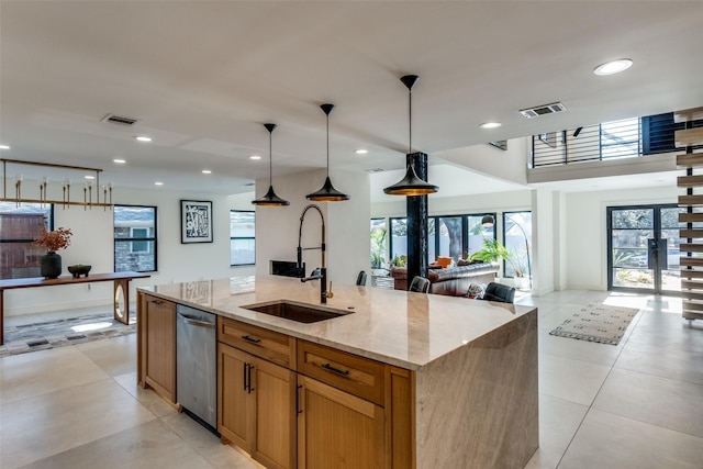 kitchen featuring light stone counters, dishwasher, hanging light fixtures, a kitchen island with sink, and sink