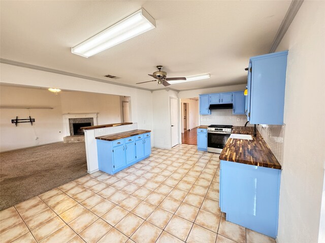 kitchen with dishwasher, stainless steel stove, sink, blue cabinets, and butcher block counters