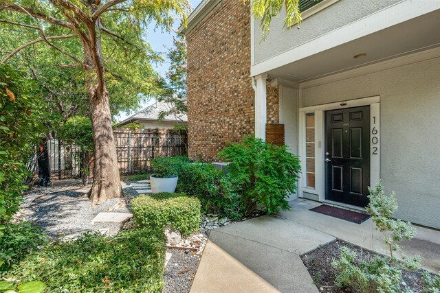 view of exterior entry featuring brick siding and fence