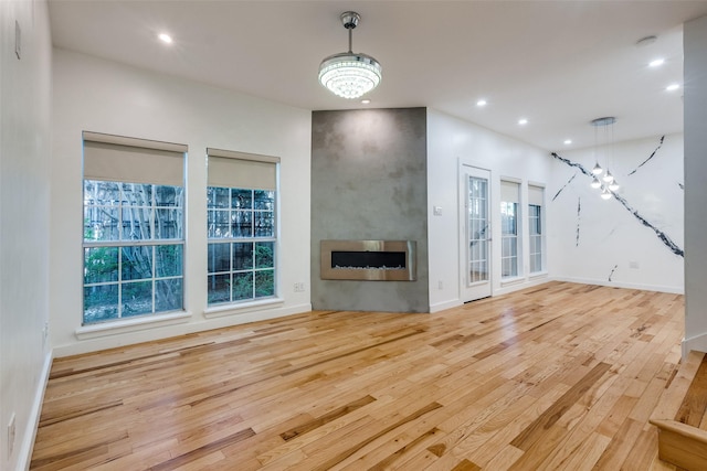 unfurnished living room with a notable chandelier, recessed lighting, a fireplace, baseboards, and light wood-style floors