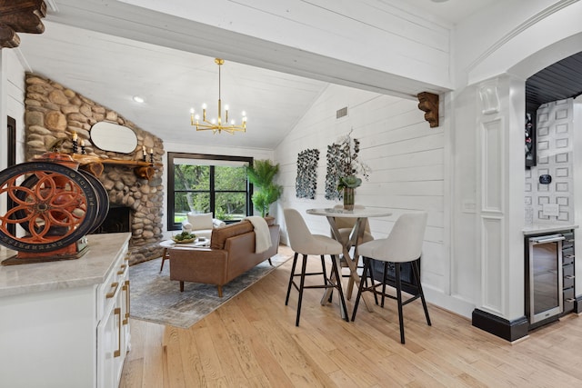 dining space with a fireplace, an inviting chandelier, lofted ceiling, light wood-type flooring, and wine cooler