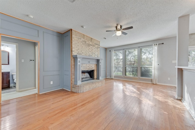 unfurnished living room with a textured ceiling, a fireplace, ceiling fan, and light hardwood / wood-style floors