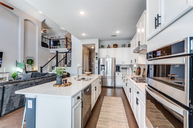 kitchen featuring sink, white cabinets, wall chimney range hood, a kitchen island with sink, and appliances with stainless steel finishes