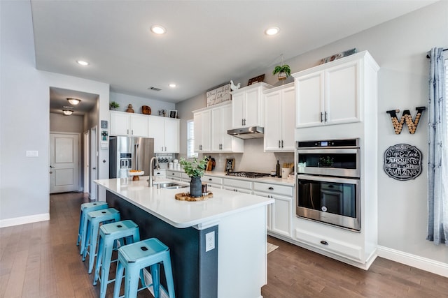 kitchen with white cabinets, dark wood-type flooring, an island with sink, and appliances with stainless steel finishes