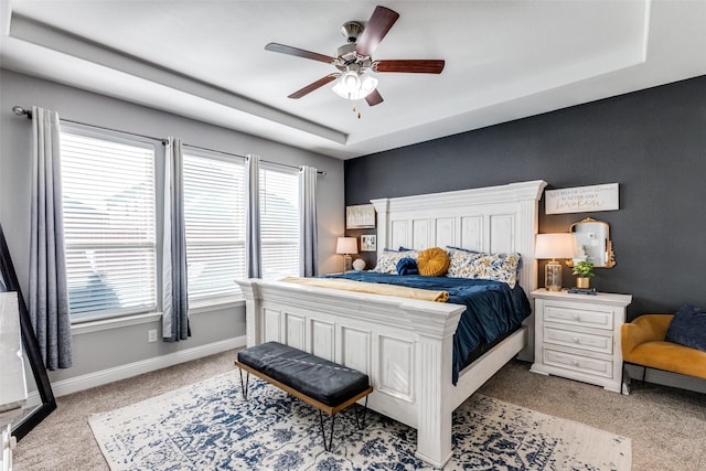 carpeted bedroom with ceiling fan and a tray ceiling